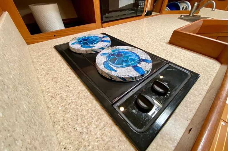 Slide: The Image of 2002 Mainship Pilot 34 galley with stove, turtle-themed covers, and countertop. - 29