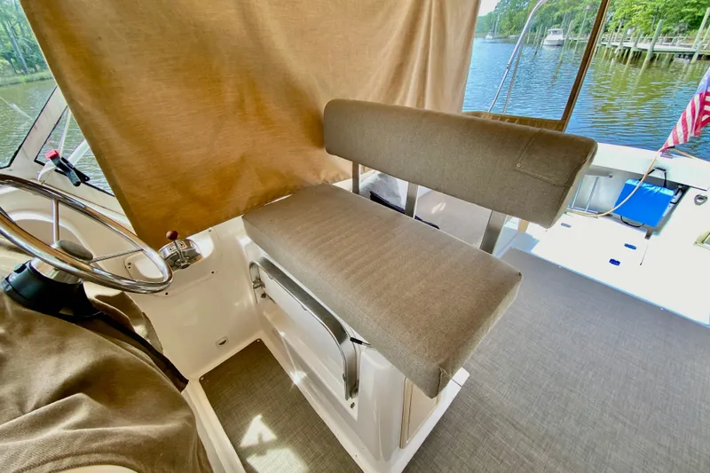 Slide: The Image of 2002 Mainship Pilot 34 helm seat with steering wheel, overlooking serene water view. - 10