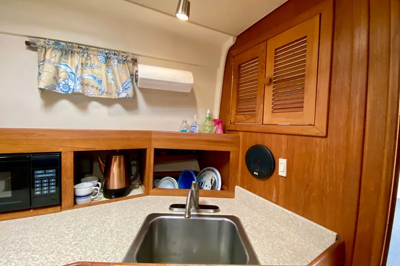 Slide: The Image of 2002 Mainship Pilot 34 kitchen with sink, microwave, and wooden cabinets. - 27