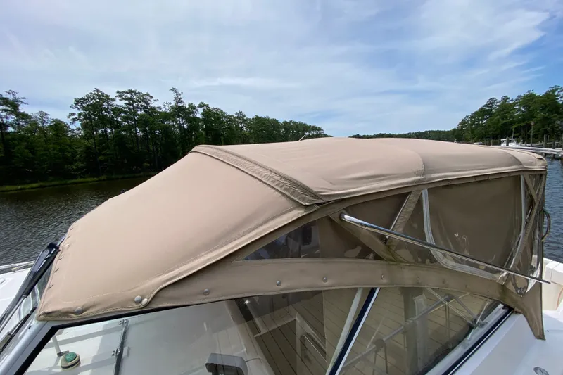 Slide: The Image of 2002 Mainship Pilot 34 boat with beige canopy, docked near a wooded shoreline. - 46