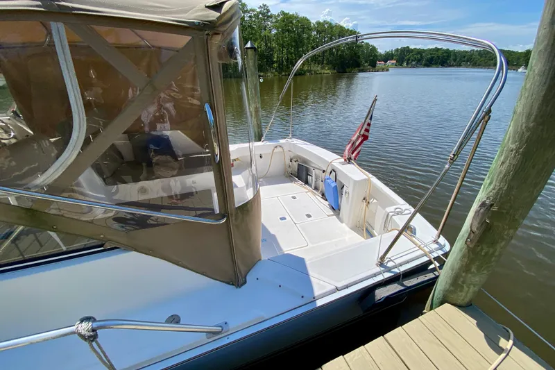 Slide: The Image of 2002 Mainship Pilot 34 docked by a serene lake with canopy and American flag. - 6