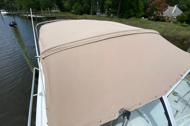 Slide: The Image of 2002 Mainship Pilot 34 boat with beige canvas cover docked by the water. - 44