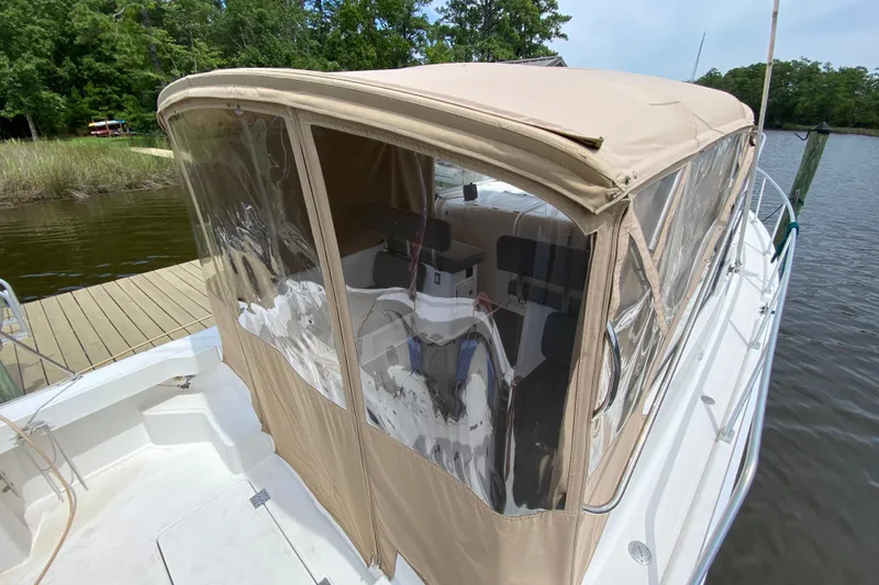 Slide: The Image of 2002 Mainship Pilot 34 boat with tan canopy docked by a serene lake. - 41