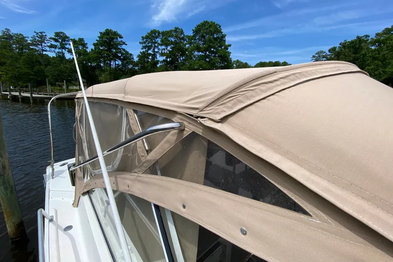 Slide: The Image of 2002 Mainship Pilot 34 boat with beige canopy docked by a serene lake. - 43