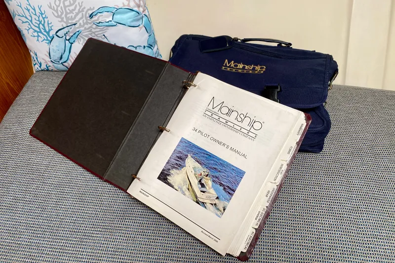 Slide: The Image of Mainship Pilot 34 owner's manual from 2002 on a cushioned seat with a branded bag. - 39