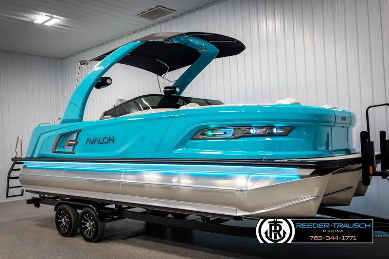 Slide: The Image of 2025 Avalon 2585 Excal VRBW pontoon boat in vibrant blue, displayed indoors on a trailer. - 2
