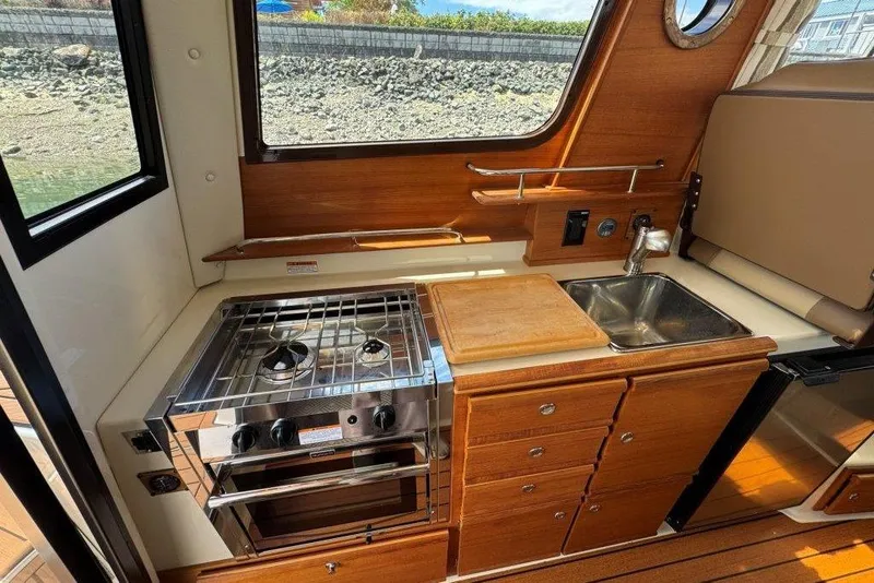 Slide: The Image of Compact kitchen in 2022 Ranger Tugs R-27 boat with stove, sink, and wooden cabinetry. - 7