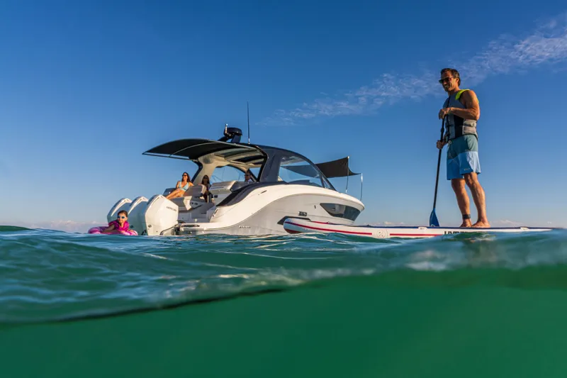 Slide: The Image of A man stands on a paddleboard next to a Sea Ray Sundancer 370 Outboard in the water. - 25