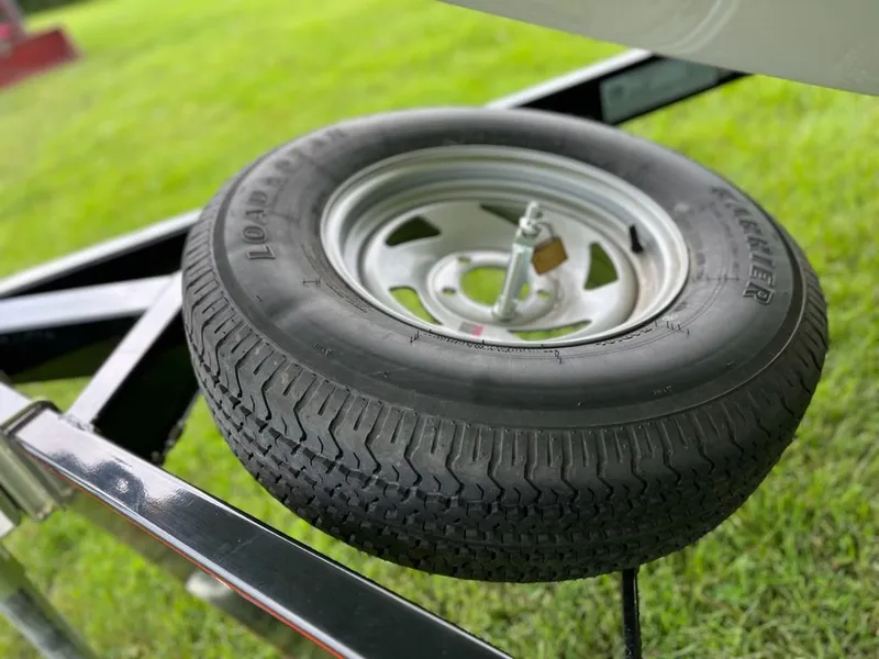Slide: The Image of A spare tire is mounted on a boat trailer, resting on grass. - 16