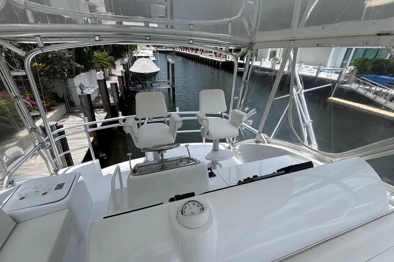 Slide: The Image of Flybridge view of 2005 Hatteras 50 Convertible yacht, featuring helm chairs and marina backdrop. - 6