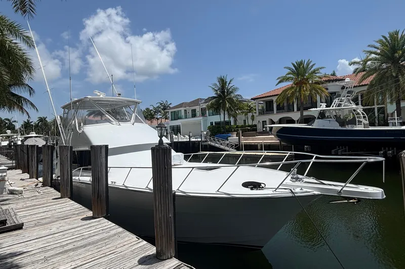 The Image of 2005 Hatteras 50 Convertible yacht docked by palm trees and waterfront homes. - 1