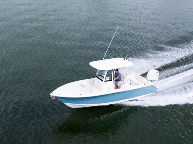 The Image of A Sea Hunt Ultra 245 SE boat speeds across the water, featuring a white and blue hull. - 1