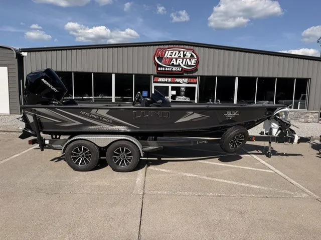 The Image of A black Lund 1875 Pro-V Bass XS boat on a trailer in front of a building. - 1