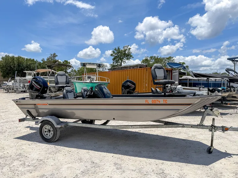 The Image of A 2022 Lowe Legacy boat on a trailer, surrounded by other boats and trees. - 1
