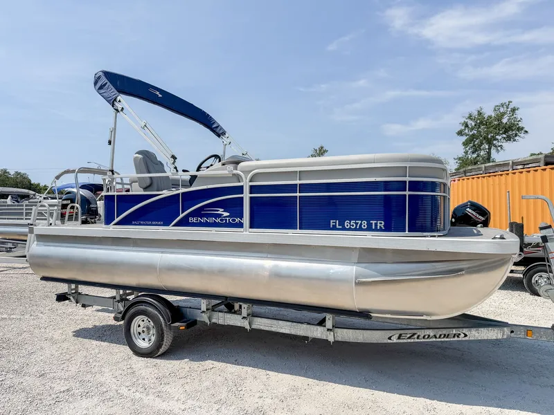 Slide: The Image of A 2024 Bennington 20 SVL pontoon boat on a trailer, featuring a blue canopy and silver hull. - 12