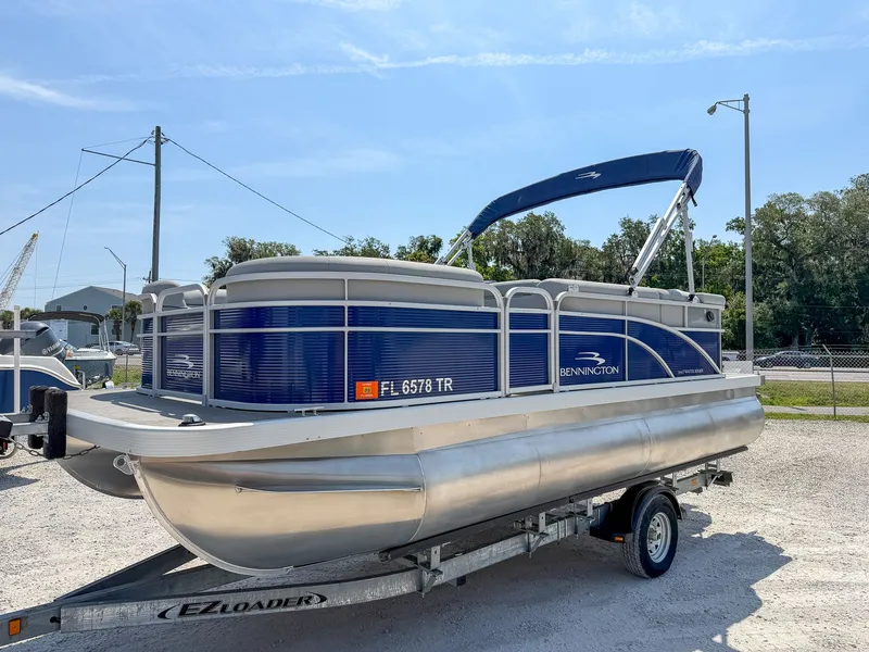 Slide: The Image of A 2024 Bennington 20 SVL pontoon boat on a trailer, featuring a blue canopy and silver details. - 11