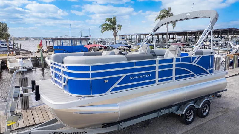 The Image of A blue Bennington pontoon boat, model 20SSRSE from 2025, sits on a trailer by the water. - 1