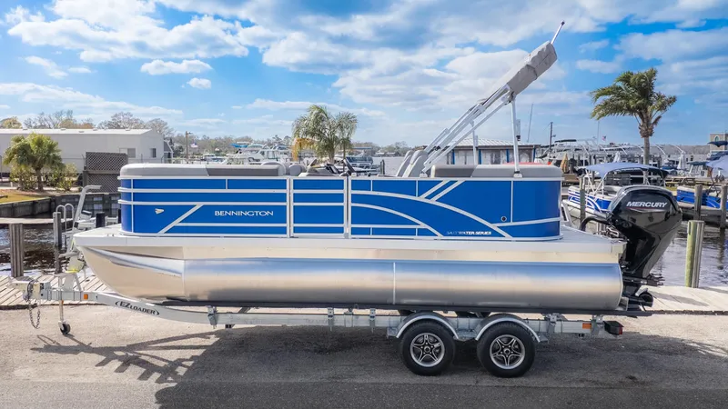 Slide: The Image of 2025 Bennington 20SSRSE pontoon boat on a trailer, featuring a blue hull and silver details. - 19