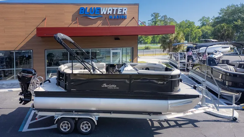 Slide: The Image of A Barletta Sanza 20L pontoon boat is on a trailer in front of a Bluewater Marine building. - 20