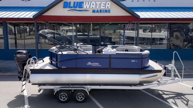 Slide: The Image of A Barletta Sanza 20L pontoon boat is on a trailer in front of a store labeled "Blue Water Marine." - 20