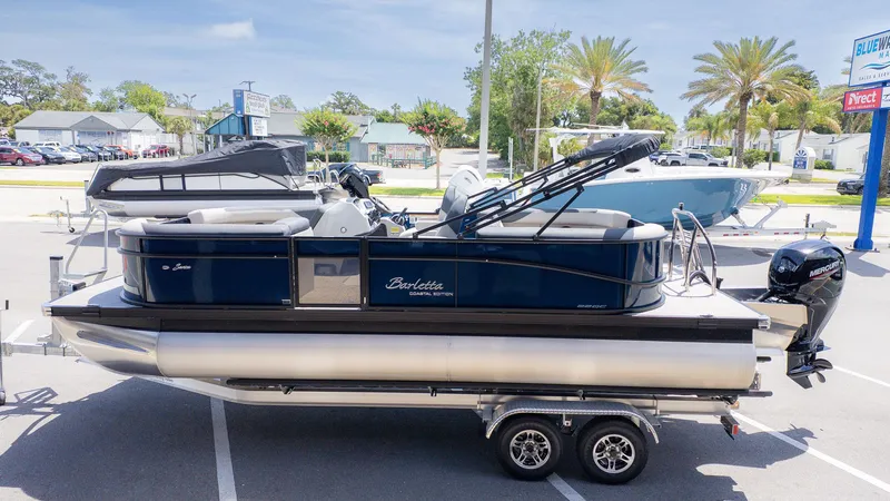 Slide: The Image of A Barletta SANZA 22QC pontoon boat on a trailer, surrounded by other boats and palm trees. - 3