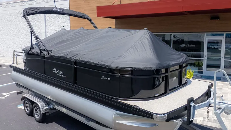 The Image of A Barletta SANZA 22QC pontoon boat with a black cover on a trailer. - 1