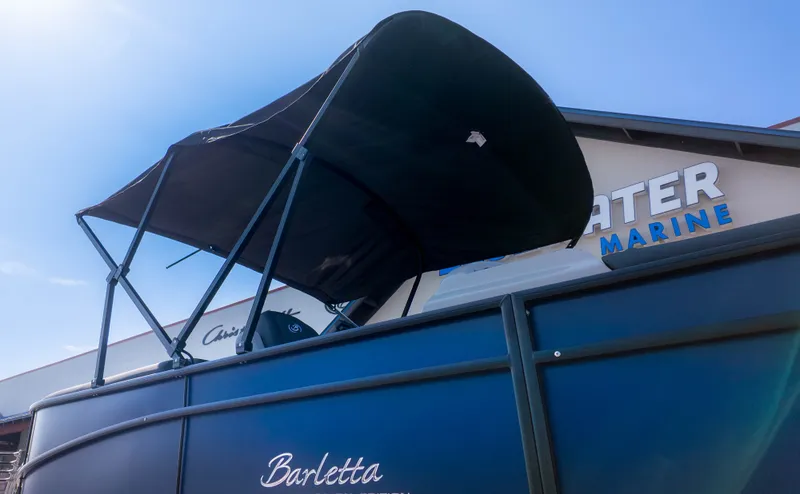 Slide: The Image of Barletta Sanza S22QC pontoon boat with black sunshade, in front of a building with marine signage. - 18