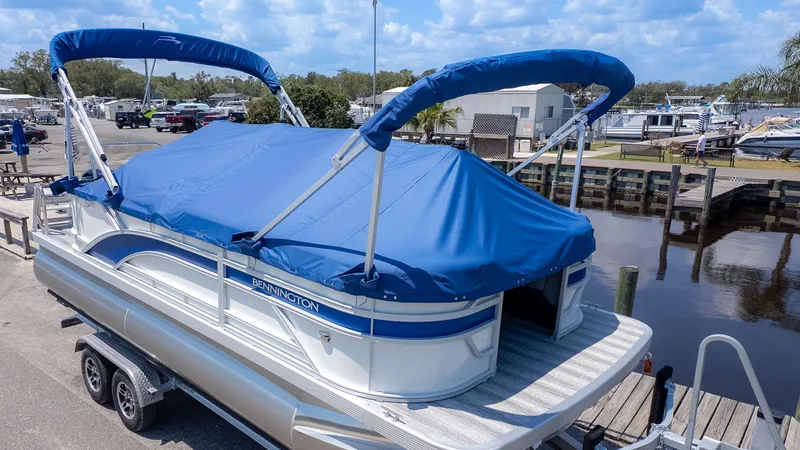 Slide: The Image of A Bennington 20 S Cruise pontoon boat with a blue cover, on a trailer at a dock. - 16