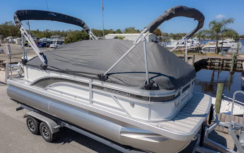 Slide: The Image of A Bennington 20 S Cruise pontoon boat with a gray cover sits on a trailer at a marina. - 18