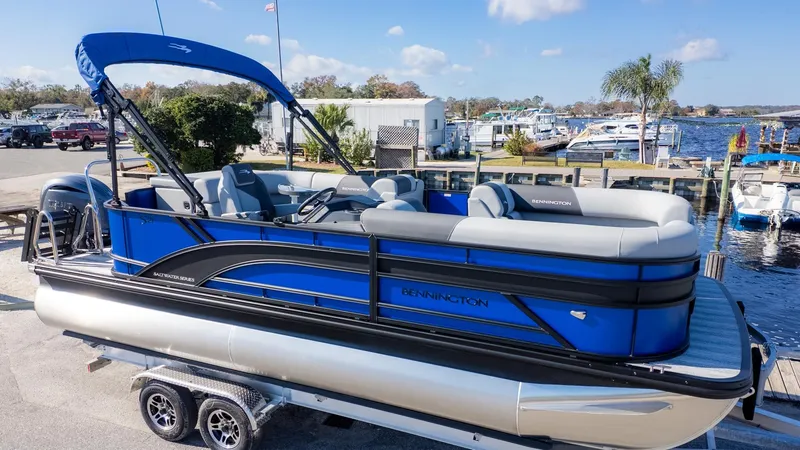 The Image of A blue Bennington pontoon boat with gray seats is on a trailer near a marina. - 1