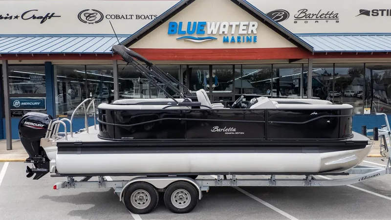 Slide: The Image of A Barletta ARIA 22QC pontoon boat on a trailer in front of a boat dealership. - 23