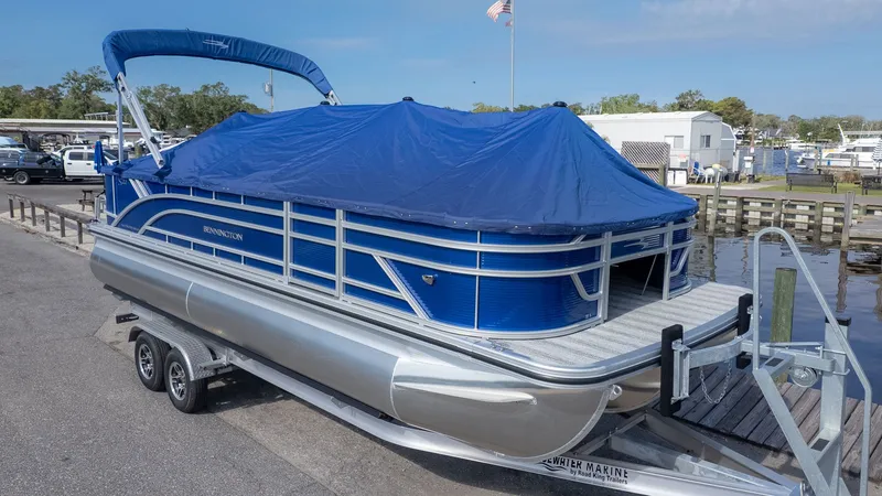 Slide: The Image of A Bennington 22 S 4 PT Fishing pontoon boat with a blue cover on a trailer at the dock. - 21