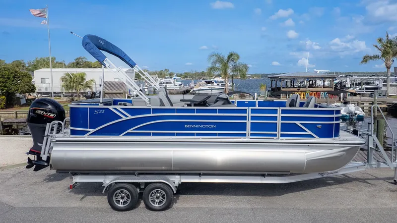 Slide: The Image of Bennington 22 S 4 PT Fishing pontoon boat on a trailer, featuring a blue canopy and motor. - 19