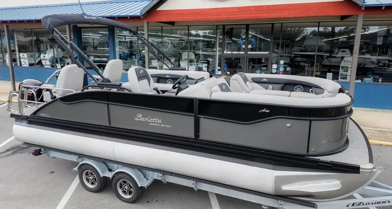 Slide: The Image of The image shows a 2026 Barletta Aria A22CC pontoon boat on a trailer in front of a store. - 25