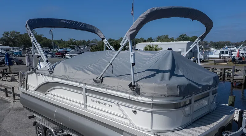 The Image of A Bennington 21 S Swingback pontoon boat with a gray cover, on a trailer on land. - 1