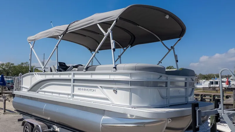 Slide: The Image of 2026 Bennington 21 S Swingback pontoon boat with gray canopy, parked on a trailer. - 22