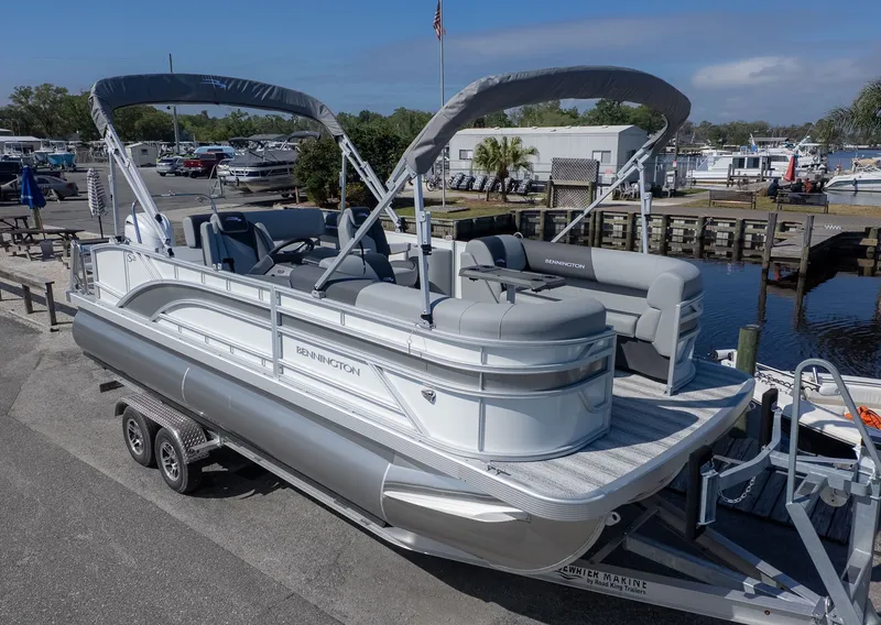 The Image of A modern pontoon boat with gray upholstery and two bimini tops, on a trailer on land. - 1