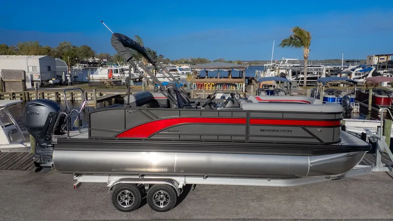 Slide: The Image of A Bennington 22 S Swingback pontoon boat on a trailer, featuring a red and gray design, at a marina. - 18