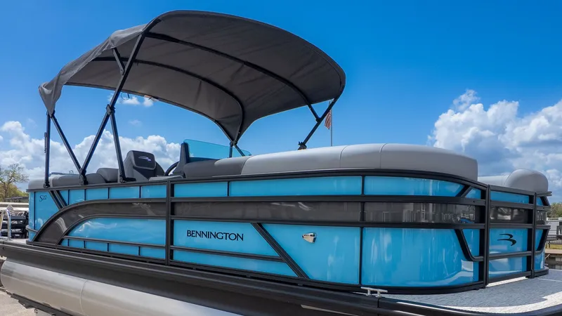 Slide: The Image of A modern Bennington pontoon boat with a blue hull and black canopy, on a trailer. - 24