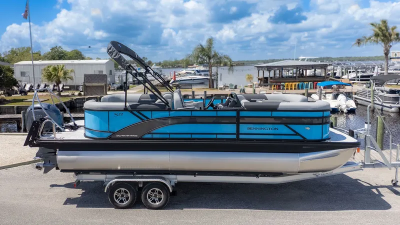 Slide: The Image of A Bennington 22 S STERN RADIUS pontoon boat on a trailer, set against a marina with palm trees. - 22