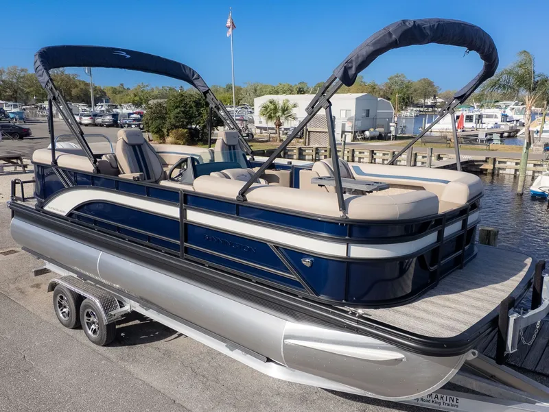 The Image of A sleek Bennington pontoon boat with blue accents, on a trailer at a sunny marina. - 1