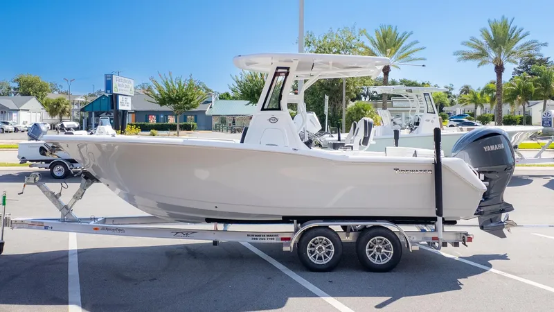 The Image of A white Tidewater 232 LXF boat on a trailer, parked in a lot under sunny weather. - 1