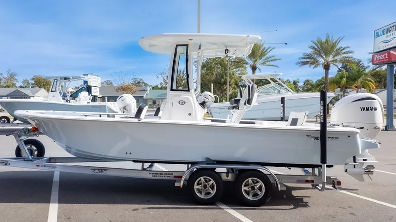 The Image of A Tidewater 2300 Carolina Bay boat on a trailer, surrounded by palm trees and other boats. - 1