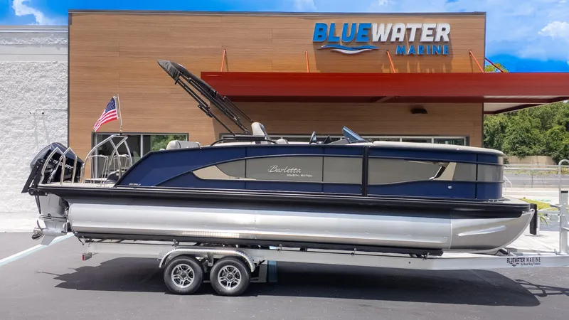 Slide: The Image of A sleek Barletta Lusso 23U pontoon boat sits on a trailer outside a Bluewater Marine building. - 30