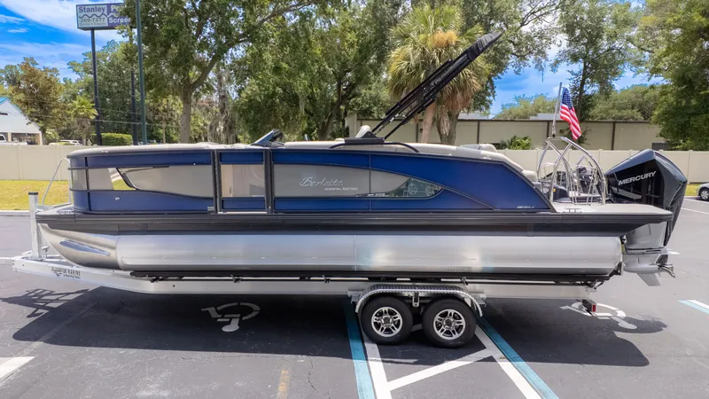 Slide: The Image of A 2026 Barletta Lusso 23U pontoon boat on a trailer, surrounded by trees and a parking lot. - 3