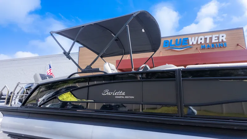 The Image of A Barletta Lusso L23M pontoon boat with a sunshade, in front of a building labeled "Bluewater Marine." - 1