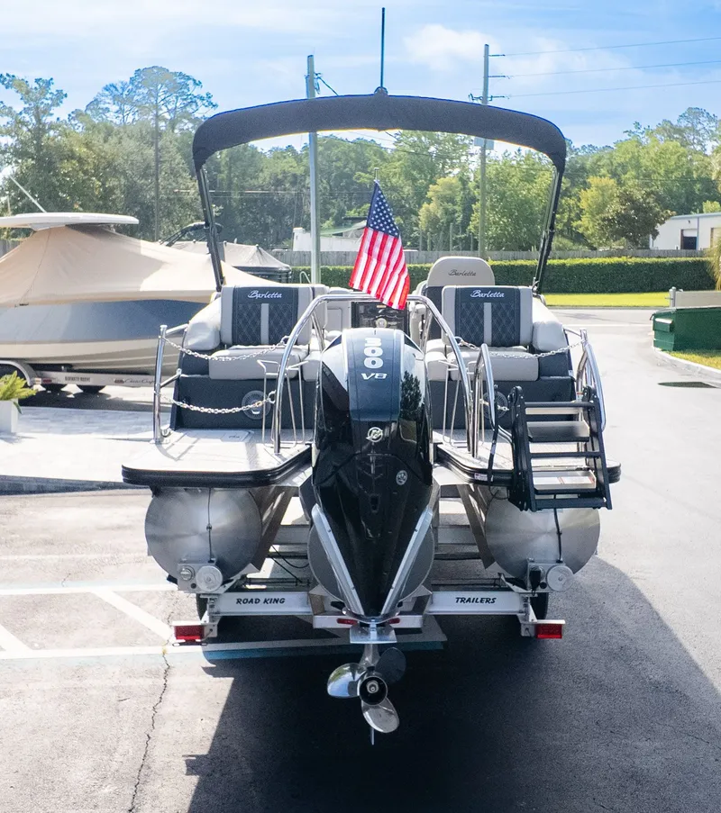Slide: The Image of The image shows a Barletta Lusso L23M pontoon boat on a trailer. It features a black canopy and an American flag. - 4