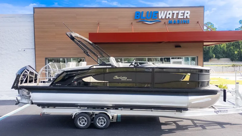 Slide: The Image of A sleek Barletta Lusso L23M pontoon boat on a trailer in front of a marine store. - 24