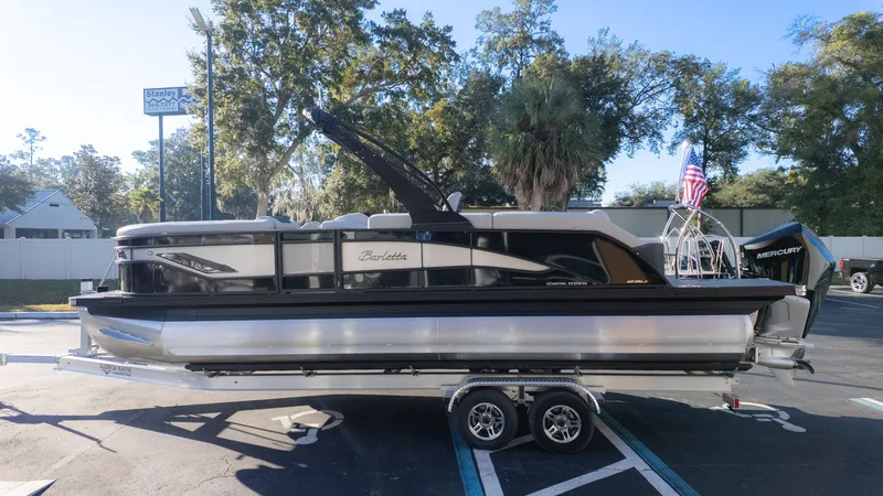 Slide: The Image of A 2026 Barletta Corsa X23U pontoon boat on a trailer, surrounded by trees. - 4