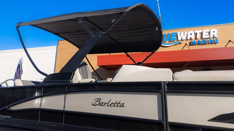 Slide: The Image of Barletta Corsa X23U pontoon boat with black sunshade, in front of a building with 'Bluewater Marine' sign. - 25